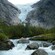 A rocky stream flowing through the mountains with the Briksdal Glacier in the background